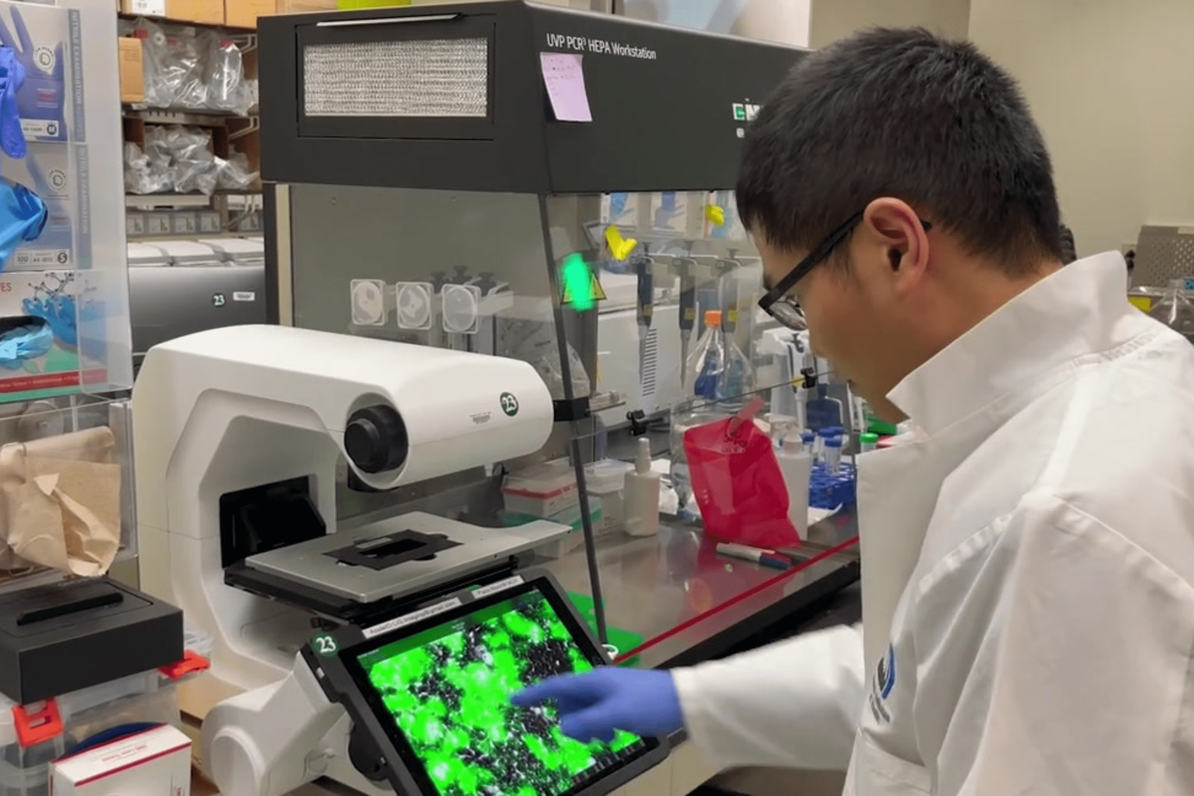 Joshua Tan, Ph.D. analyzing lab data through a microscope.